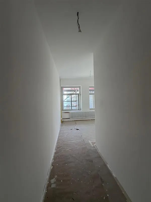Langer Flur mit glatten weissen Wänden und einem Fenster am Ende